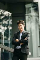 confidente asiático hombre con un sonrisa en pie participación bloc y tableta a el moderno oficina. foto
