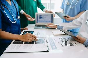 Medical team having a meeting with doctors in white lab coats and surgical scrubs seated at a table discussing a patients working online using computers in medical industry photo