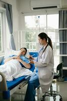 médico que se discute tratamiento con masculino paciente hablando y riendo sentado en examen cama en clínica o hospital foto