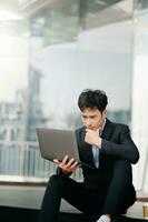 Young Asian business man working at outside business center with laptop, tablet, smartphone and taking notes on the paper. photo