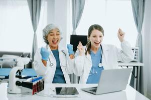 Medical team having a meeting with doctors in white lab coats and surgical scrubs seated at a table discussing a patients working online using computers in the medical industry photo