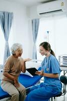 Friendly Female Head Nurse Making Rounds does Checkup on Patient Resting in Bed. She Checks tablet while Man Fully Recovering after Successful Surgery in hospital photo