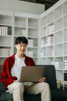 Young attractive Asian man smiling thinking planning writing in notebook, tablet and laptop working from home  at home office photo