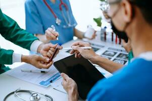 Medical team having a meeting with doctors in white lab coats and surgical scrubs seated at a table discussing a patients working online using computers photo