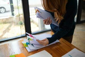 secretary searches through stacked documents on desk in office to find lease within stacked documents just before meeting. concept difficulty in finding hire purchase contract from stacked documents photo