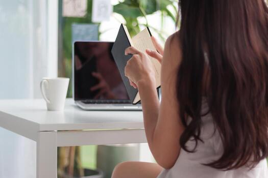 young woman wearing white see through pajamas sits and reads book to review lessons in morning to understand and learn lessons from books because exam time is near. concept of reading books to learn photo