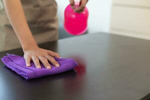 Cleaning staff is wiping cloth with cleaner and disinfectant on the surface of table to make the table clean with cleaning products and free from germs clinging to surface of the table in living room. photo