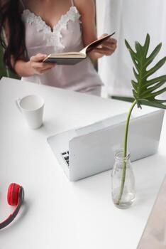 young woman wearing white see through pajamas sits and reads book to review lessons in morning to understand and learn lessons from books because exam time is near. concept of reading books to learn photo