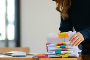secretary searches through stacked documents on desk in office to find lease within stacked documents just before meeting. concept difficulty in finding hire purchase contract from stacked documents photo