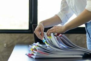 secretary searches through stacked documents on desk in office to find lease within stacked documents just before meeting. concept difficulty in finding hire purchase contract from stacked documents photo