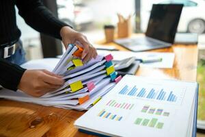 secretary searches through stacked documents on desk in office to find lease within stacked documents just before meeting. concept difficulty in finding hire purchase contract from stacked documents photo