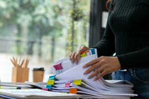secretary searches through stacked documents on desk in office to find lease within stacked documents just before meeting. concept difficulty in finding hire purchase contract from stacked documents photo