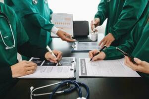 Medical team having a meeting with doctors in white lab coats and surgical scrubs seated at a table discussing a patients working online using computers in the medical industry photo
