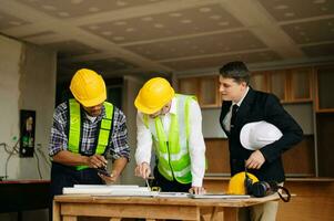 Contractor and architect looking at plan, tablet, laptop and talking about working on big project. Building in construction process photo