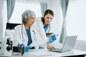 Medical team having a meeting with doctors in white lab coats and surgical scrubs seated at a table discussing a patients working online using computers in the medical industry photo
