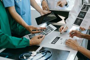 Medical team having a meeting with doctors in white lab coats and surgical scrubs seated at a table discussing a patients working online using computers in the medical industry photo