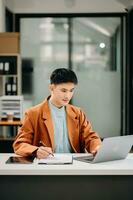 joven asiático negocio hombre trabajando a oficina con computadora portátil, tableta y tomando notas en el papel. foto