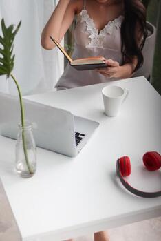 young woman wearing white see through pajamas sits and reads book to review lessons in morning to understand and learn lessons from books because exam time is near. concept of reading books to learn photo