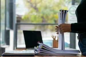 secretary searches through stacked documents on desk in office to find lease within stacked documents just before meeting. concept difficulty in finding hire purchase contract from stacked documents photo