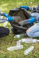 Two man employees use black garbage bags to collect plastic bottles and recyclable waste from the lawn and sidewalks for recycling. Concept of sorting plastic waste for recycling photo