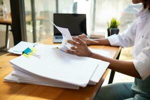 secretary searches through stacked documents on desk in office to find lease within stacked documents just before meeting. concept difficulty in finding hire purchase contract from stacked documents photo