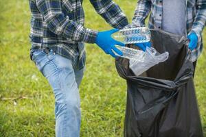 Two man employees use black garbage bags to collect plastic bottles and recyclable waste from the lawn and sidewalks for recycling. Concept of sorting plastic waste for recycling photo