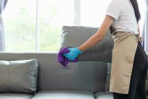 Cleaning staff is wiping cloth with cleaner and disinfectant on the surface of sofa to make the sofa clean with cleaning products and free from germs clinging to surface of the sofa in living room. photo