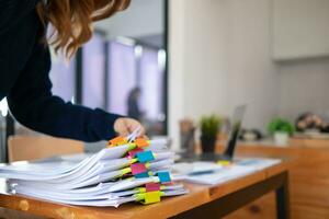 secretary searches through stacked paperwork on desk in office to find lease within stacked paperwork just before meeting. concept difficulty in finding hire purchase contract from stacked paperwork photo