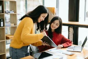 Two Attractive young Asian female college students working on the school project using laptop computer and tablet together, enjoy talking photo