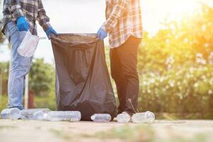 men collect plastic bottles on lawns and walkways in park and put them in bags to help keep them clean They can also collect plastic bottles for recycling. reducing environmental problems by recycling photo