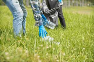Two man employees use black garbage bags to collect plastic bottles and recyclable waste from the lawn and sidewalks for recycling. Concept of sorting plastic waste for recycling photo