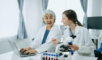 Two scientist or medical technician working, having a medical discuss meeting with an Asian senior female scientist supervisor in the laboratory with online reading, test samples and innovation photo