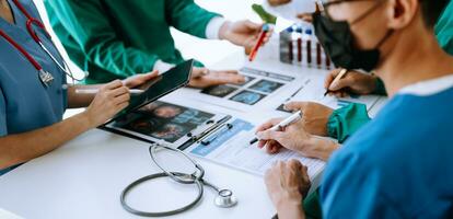 Medical team having a meeting with doctors in white lab coats and surgical scrubs seated at a table discussing a patients working online using computers photo