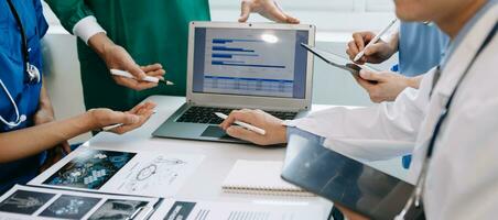 Medical team having a meeting with doctors in white lab coats and surgical scrubs seated at a table discussing a patients working online using computers in medical industry photo