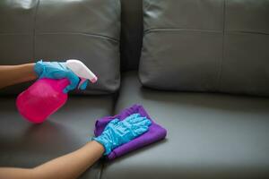 Cleaning staff is wiping cloth with cleaner and disinfectant on the surface of sofa to make the sofa clean with cleaning products and free from germs clinging to surface of the sofa in living room. photo