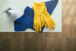 azul toalla y amarillo guantes fueron metido en de madera mesa para limpieza personal a utilizar a limpiar y evitar limpiador desde dermatitis. concepto de elegir limpieza empresa a limpiar el oficina foto