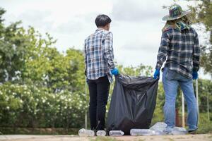 Two man employees use black garbage bags to collect plastic bottles and recyclable waste from the lawn and sidewalks for recycling. Concept of sorting plastic waste for recycling photo