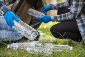 Two man employees use black garbage bags to collect plastic bottles and recyclable waste from the lawn and sidewalks for recycling. Concept of sorting plastic waste for recycling photo