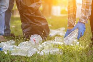Two man employees use black garbage bags to collect plastic bottles and recyclable waste from the lawn and sidewalks for recycling. Concept of sorting plastic waste for recycling photo