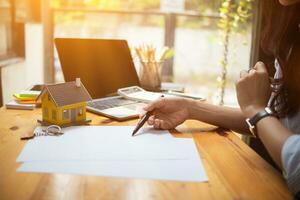 The real estate agent is reviewing the documents and calculating the interest rate to inform the tenant of the monthly installments to be paid before the real estate purchase agreement is finalized. photo