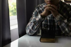 young man was praying to God in front of Bible with faith and power of faith in God. Bible study concept to understand and pray to God with faith in teachings of the Bible studied. Copy Space photo