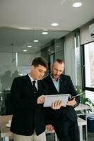 Kind leader executive manager share and discuss business solutions plan ideas on tablet with male marketing manager in modern office. photo