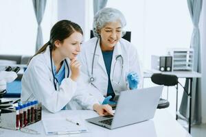 Medical team having a meeting with doctors in white lab coats and surgical scrubs seated at a table discussing a patients working online using computers in the medical industry photo