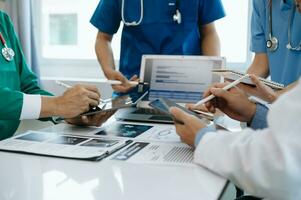 Medical team having a meeting with doctors in white lab coats and surgical scrubs seated at a table discussing a patients working online using computers in the medical industry photo