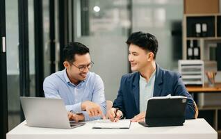 Two Asian business workers talking on the smartphone, tablet and using laptop at the office. photo