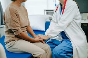 Doctor and senior  female patient who lie on the bed while checking pulse, consult and explain with nurse taking note in hospital wards or clinic. photo