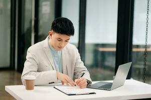 Young Asian business man working at office with laptop, tablet and taking notes on the paper. photo