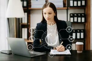 Caucasian woman sitting at a desk using a laptop computer and tablet Navigating Finance and Marketing with Technology in office with virtual icon photo