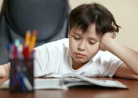 School boy studies hard over his book at home. photo