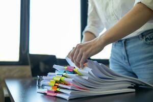 secretary searches through stacked paperwork on desk in office to find lease within stacked paperwork just before meeting. concept difficulty in finding hire purchase contract from stacked paperwork photo